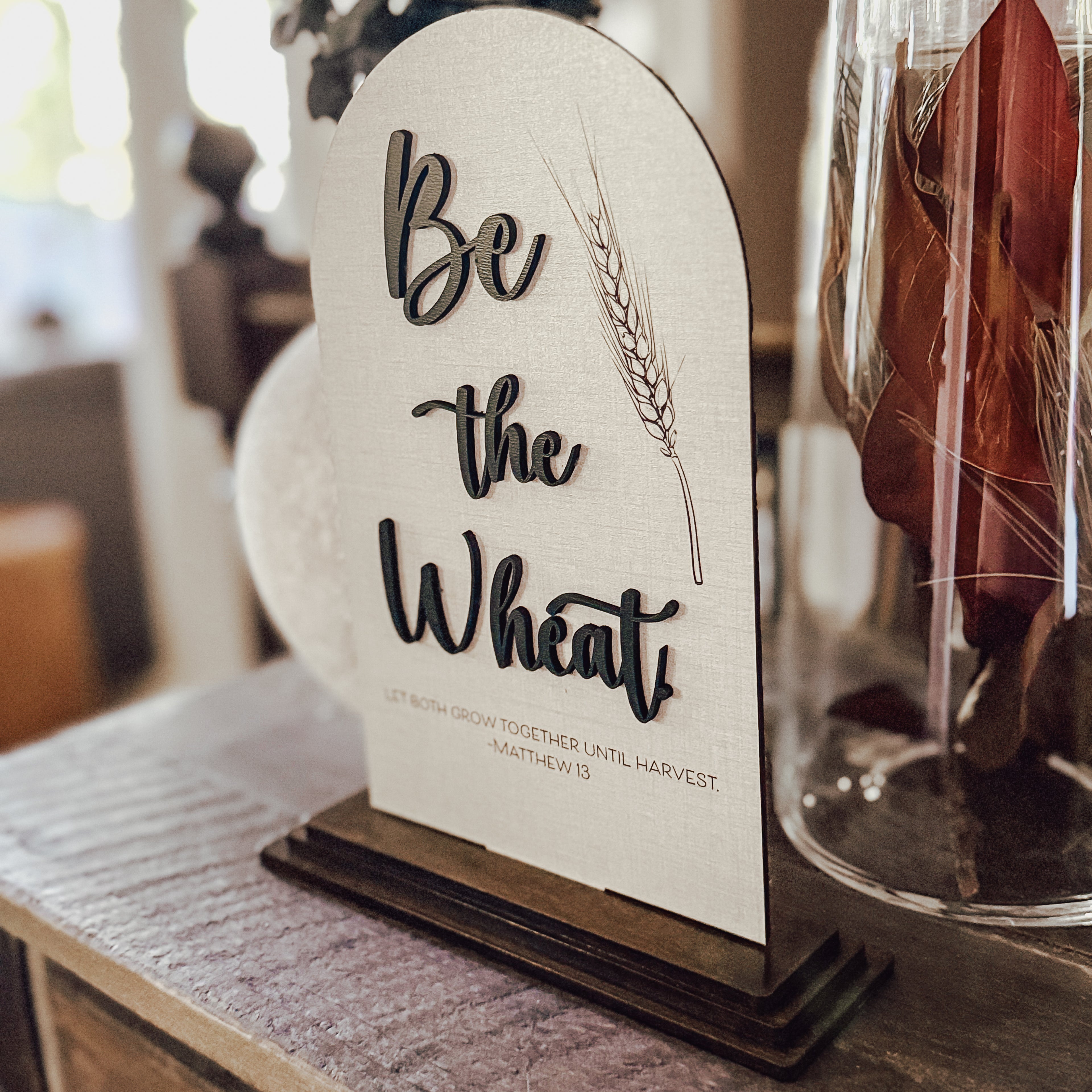 Decorative sign with 'Be the Wheat' text on a stand, blurred background