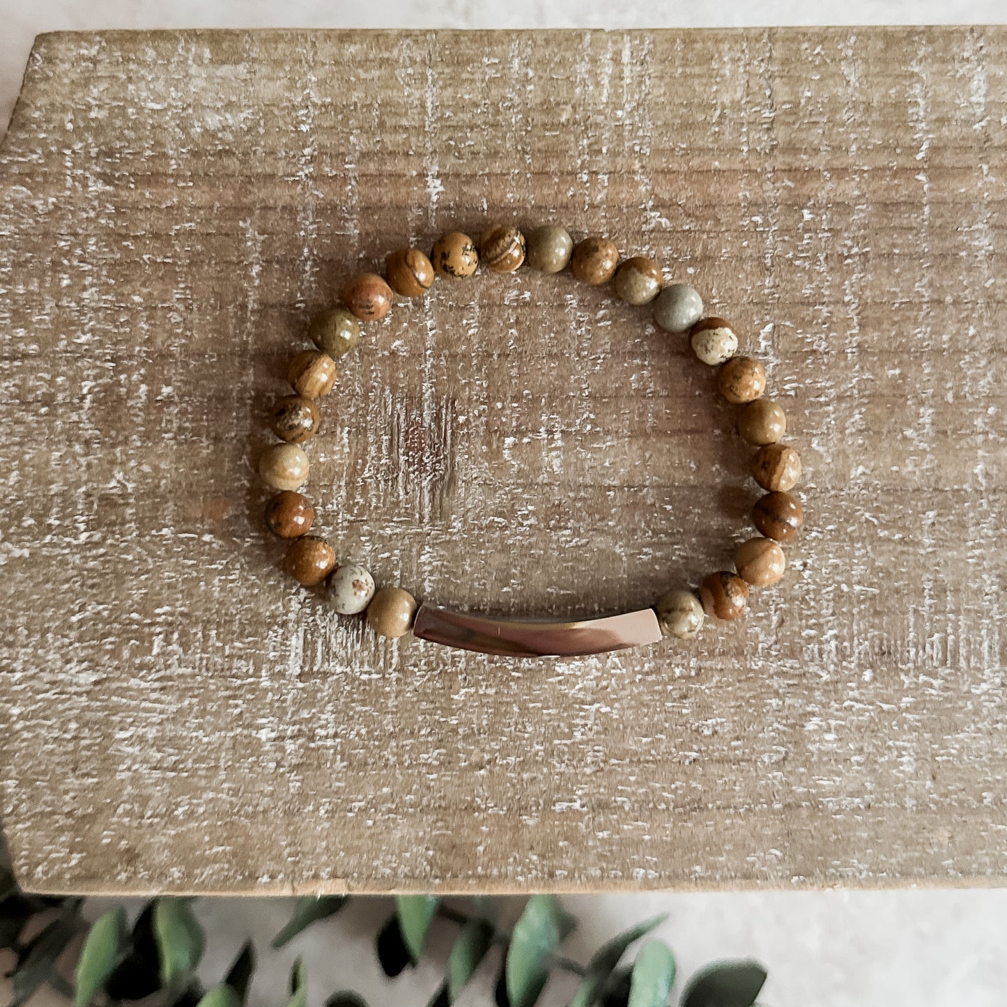 Natural jasper bracelet on a rustic wood surface with leafy greenery peeking in.