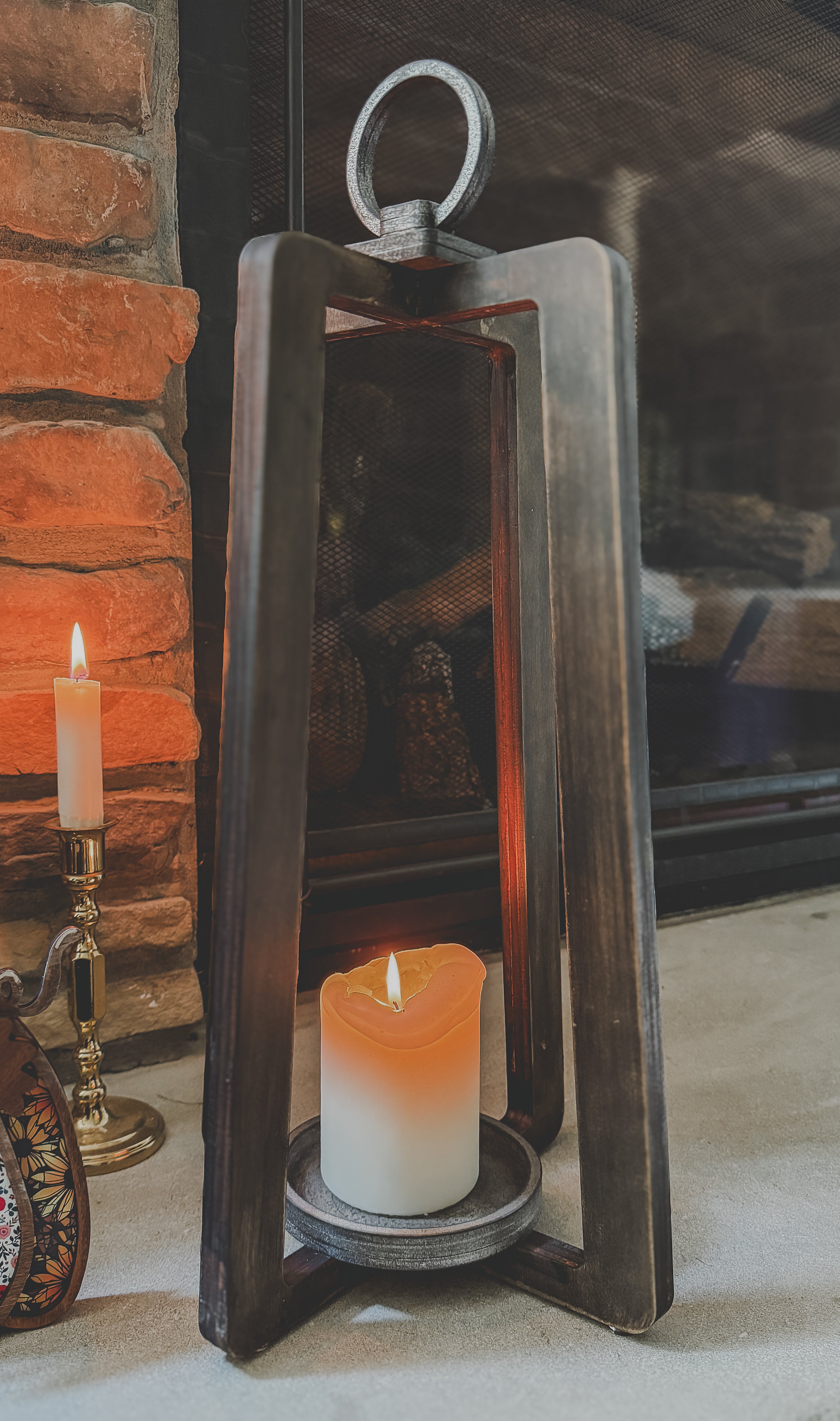 Decorative lantern with a candle inside, placed against a stone fireplace.