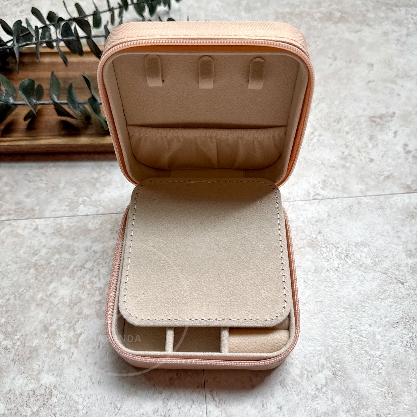 Open beige jewelry case on a light gray surface with a plant in the background