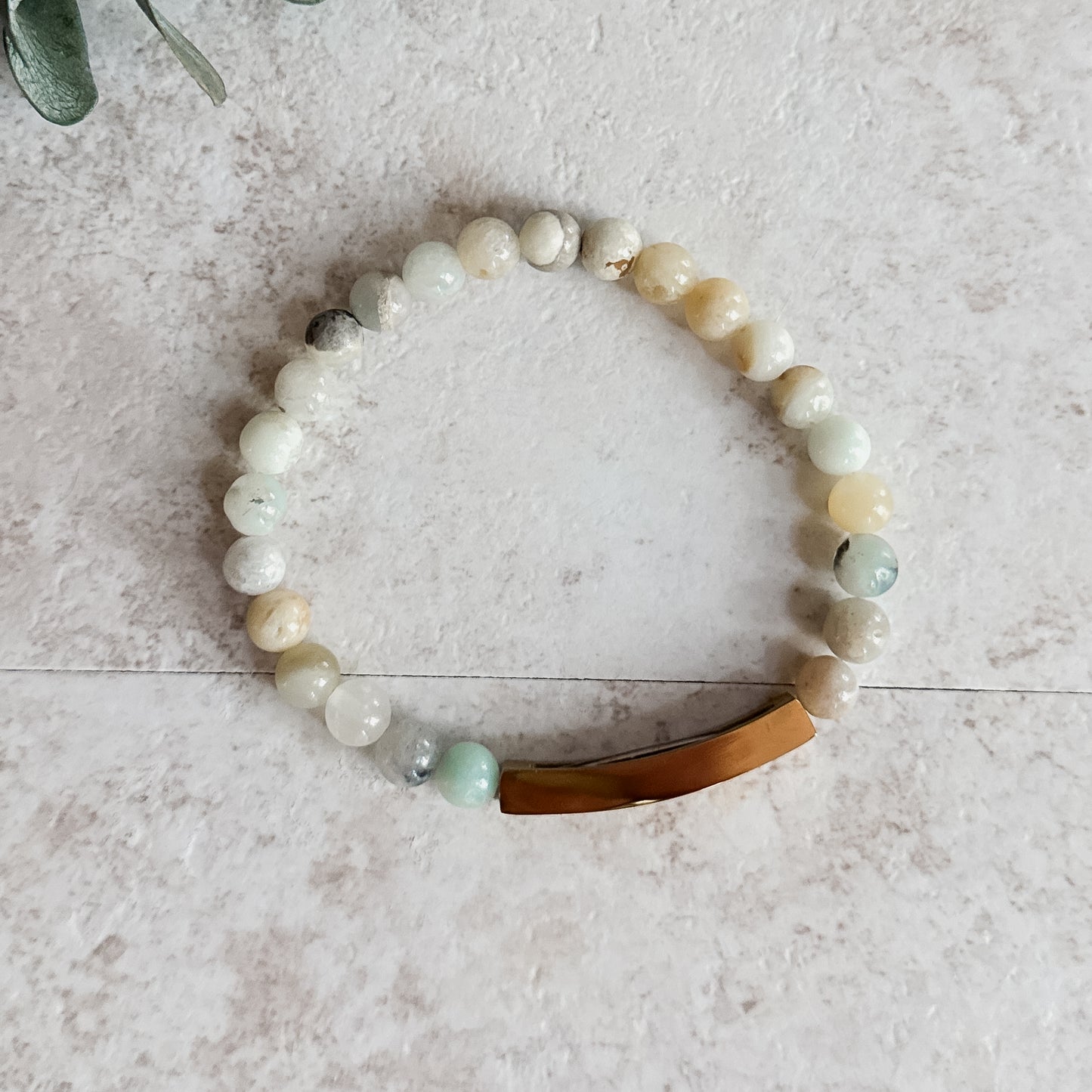 Side view of Amazonite bead bracelet with curved gold engraved bar on light stone surface