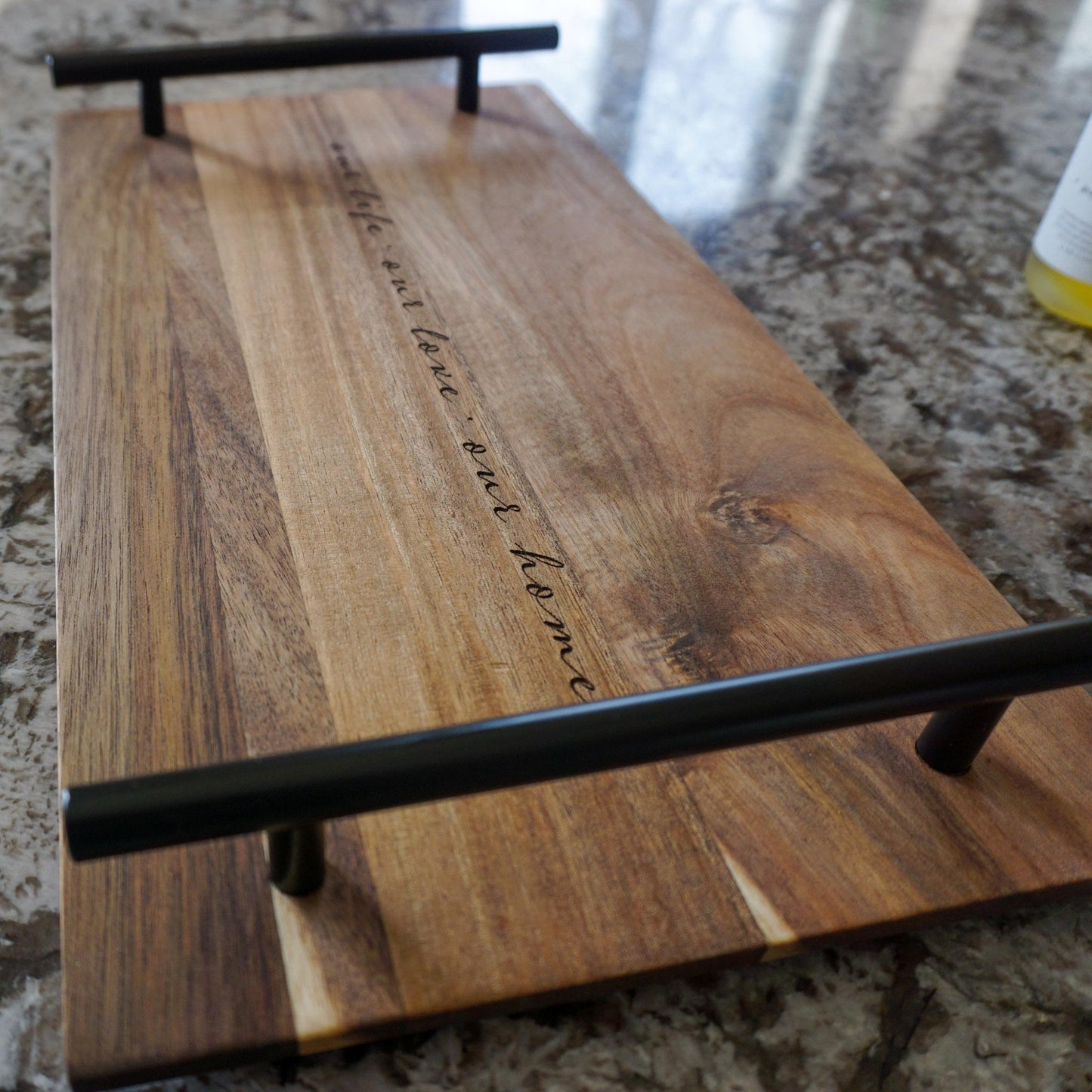 Acacia wood tray with engraved quote and black handles, styled on a kitchen countertop with natural light