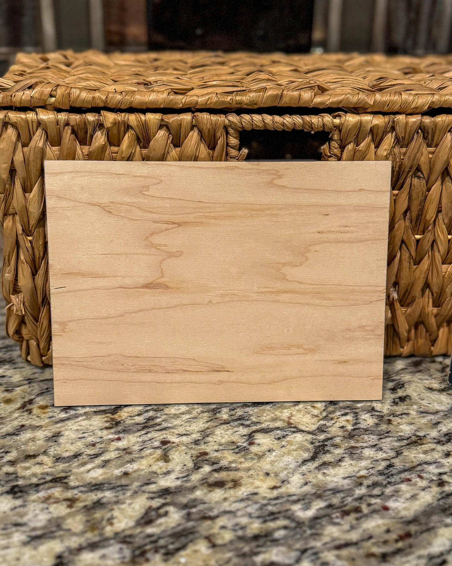 Back of the engraved wooden recipe card showing the natural woodgrain, placed on a granite surface in front of a wicker basket