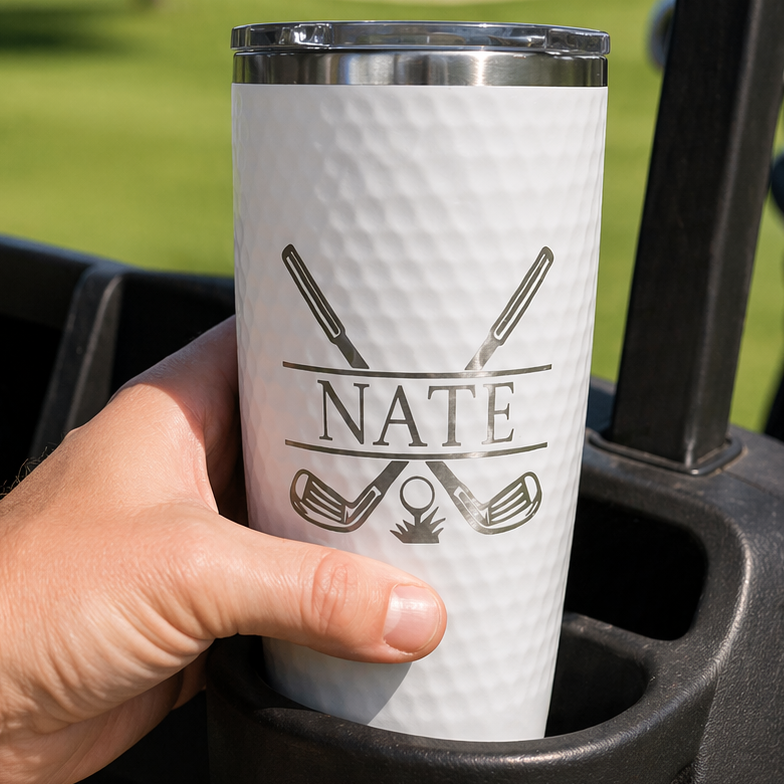 Person holding a white tumbler with 'NATE' branding in a golf cart on a golf course.