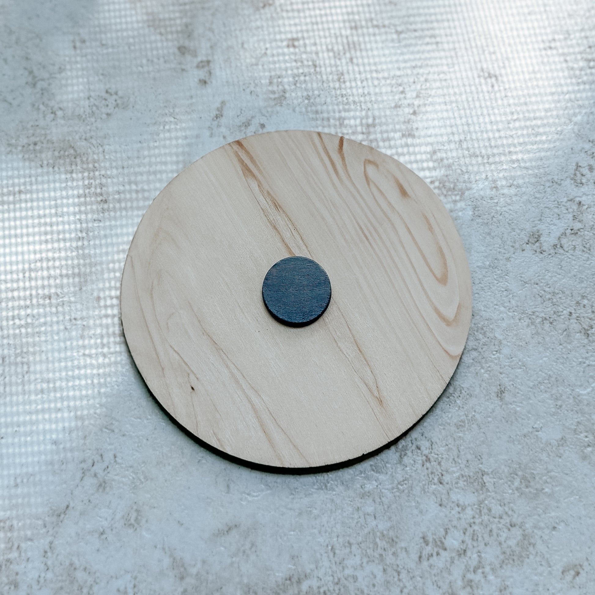 The back view of a round wooden dishwasher magnet with a central circle magnet on the back of maple.
