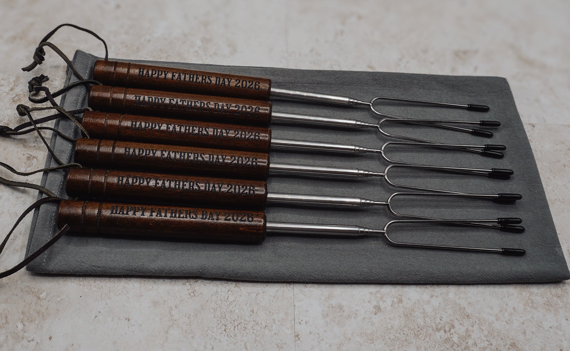 Set of 6 metal skewers with wooden handles, engraved 'Happy Father's Day 2020', on a gray mat.