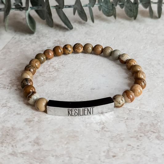 Close-up of jasper bracelet with "RESILIENT" engraved on a polished stainless steel tag