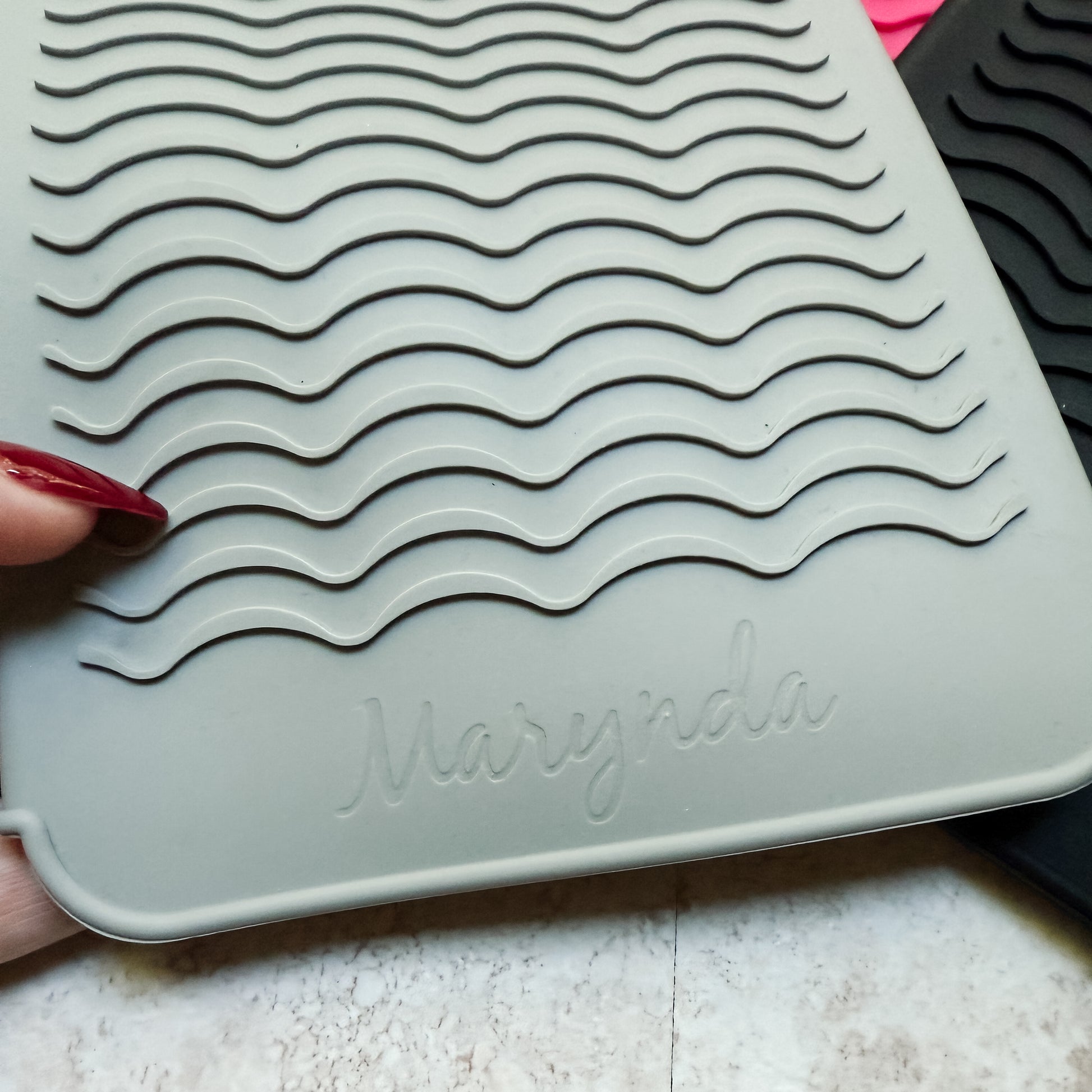 Gray silicone mat with wavy pattern and 'Marynda' branding held by a hand.