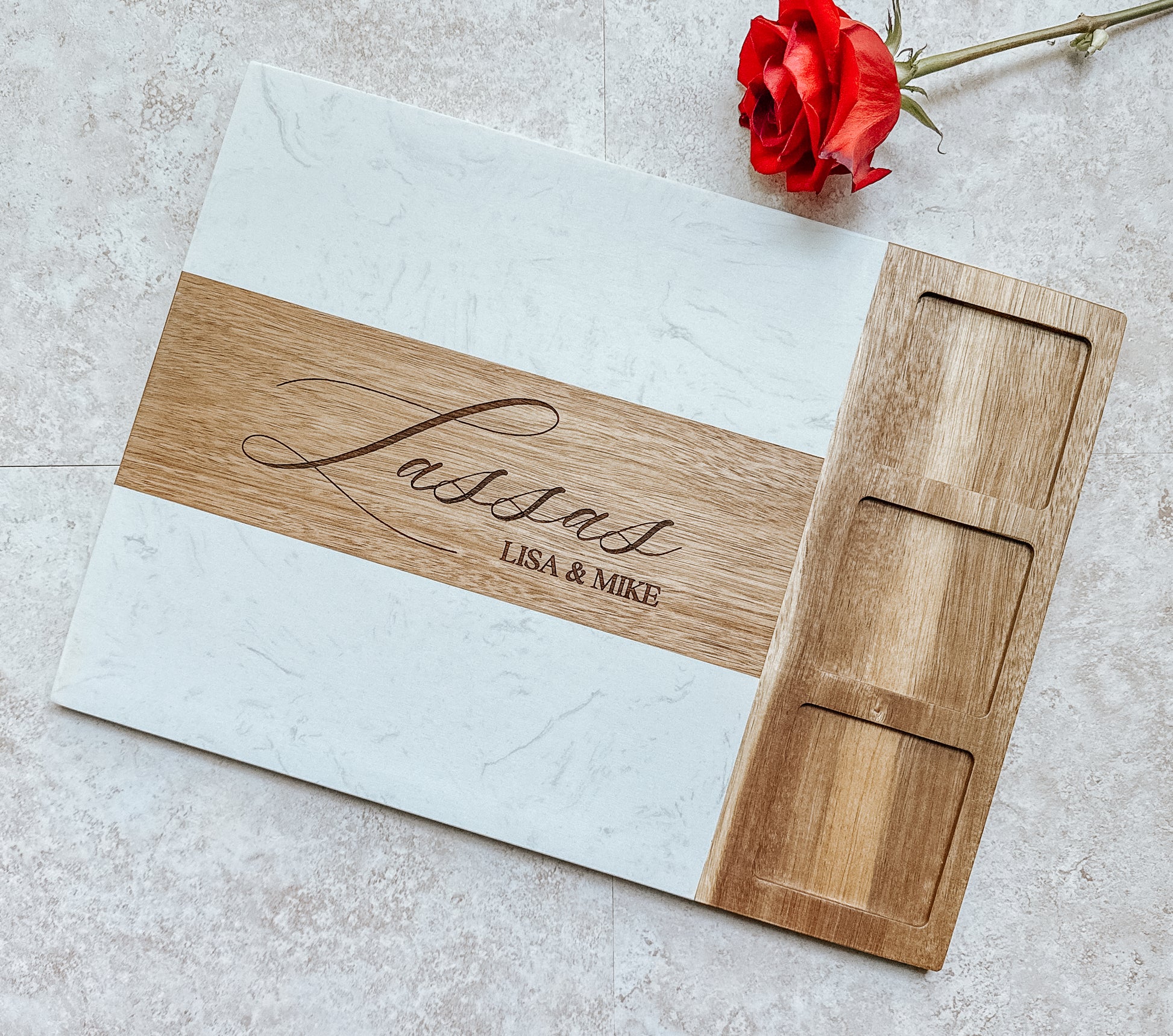 Wooden cutting board with engraved name and date on a light surface with a red rose.