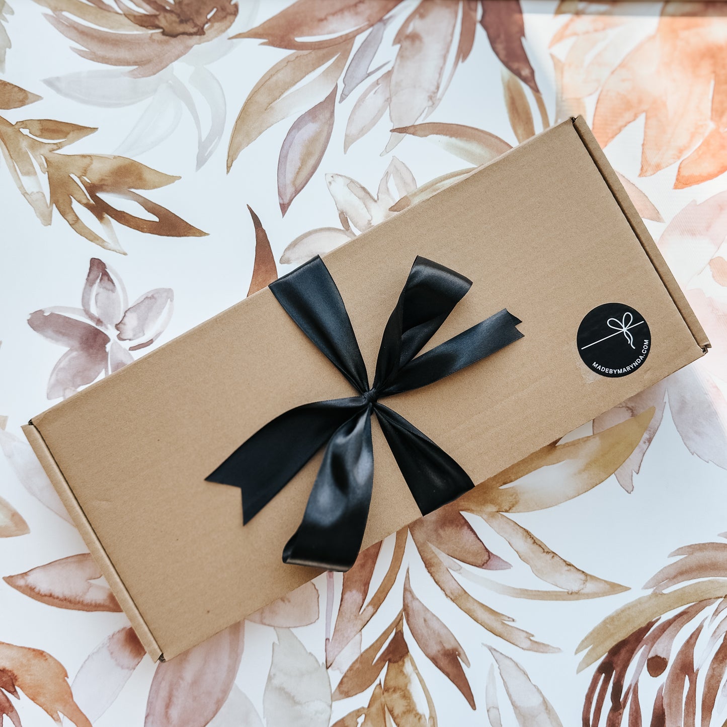 Gift box with a black ribbon on a floral-patterned background