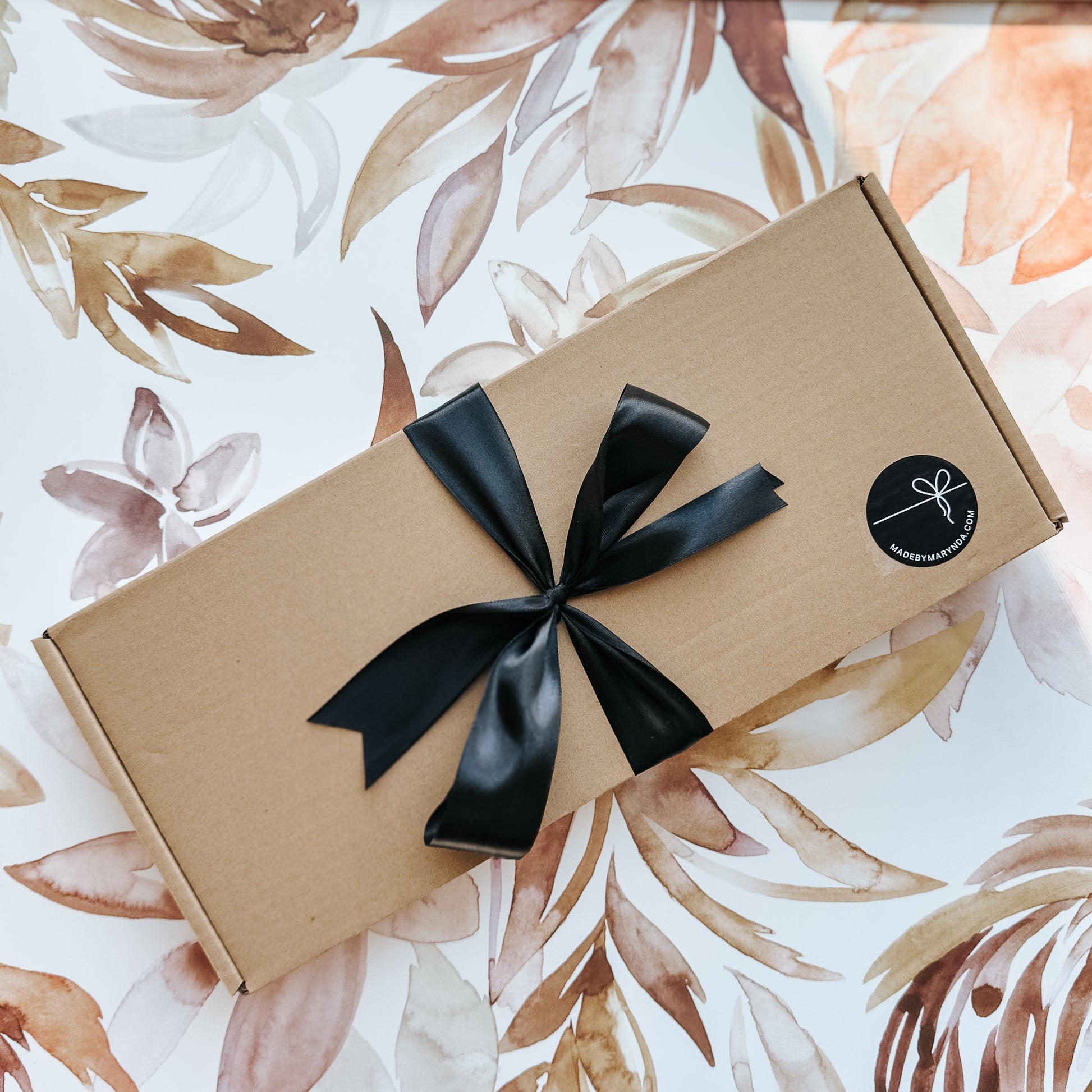 Gift box with a black ribbon on a floral-patterned background