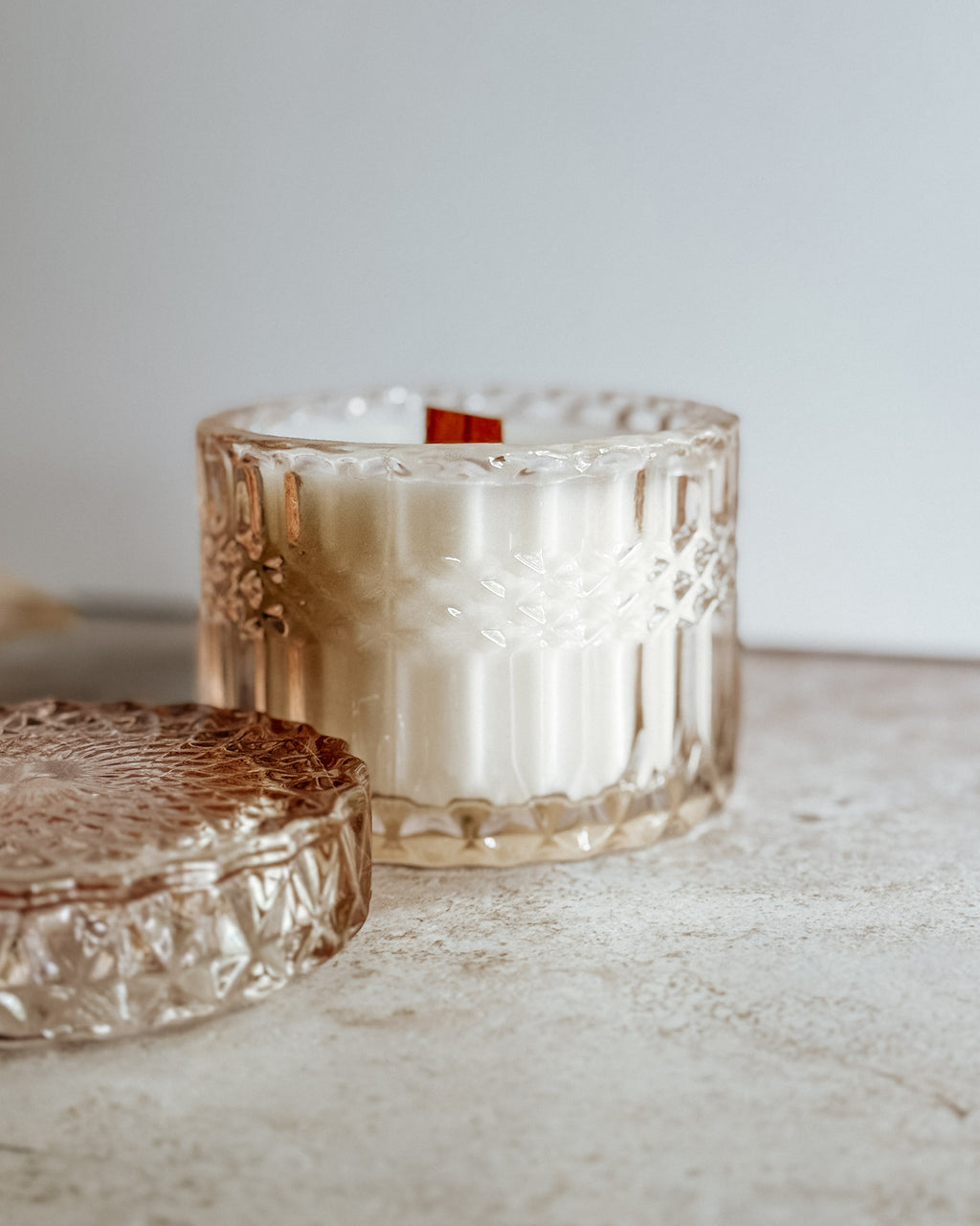 Blushing Bride candle in embossed crystal jar with wooden wick, displayed on neutral stone surface