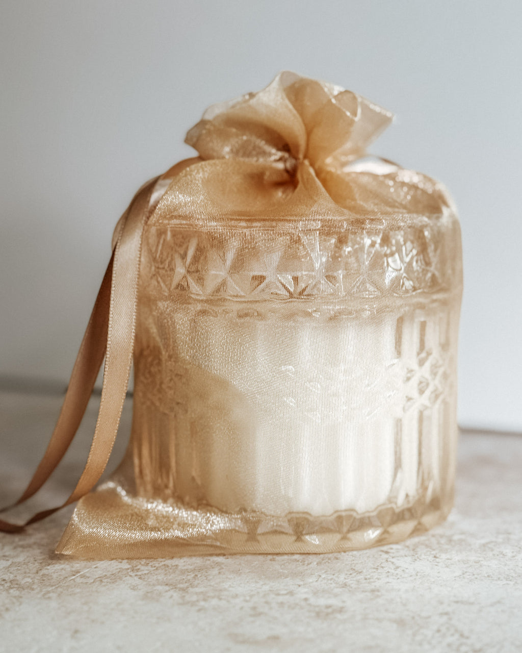 Blushing Bride candle in crystal jar wrapped in sheer gold organza gift bag with satin ribbon, light background