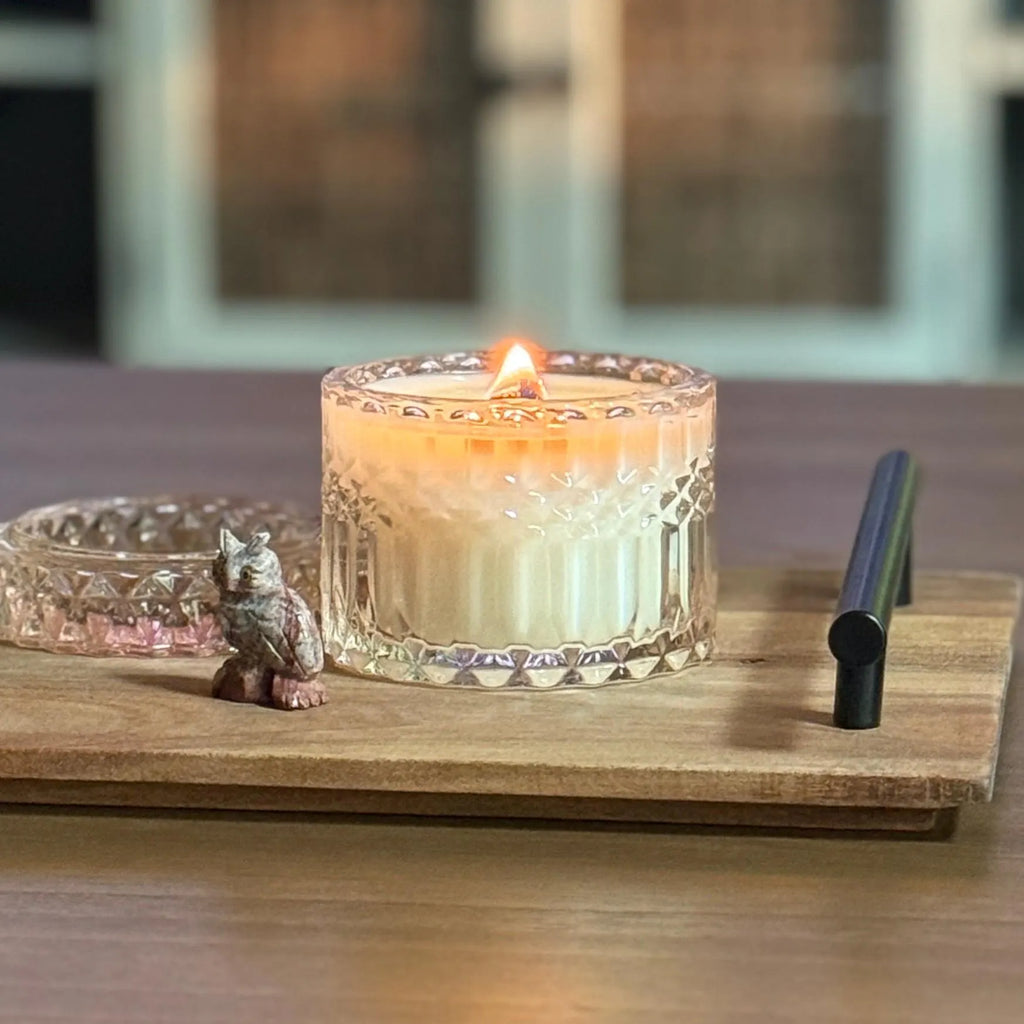 Romantic floral candle in crystal glass jar, burning on a wood tray with a small owl figurine