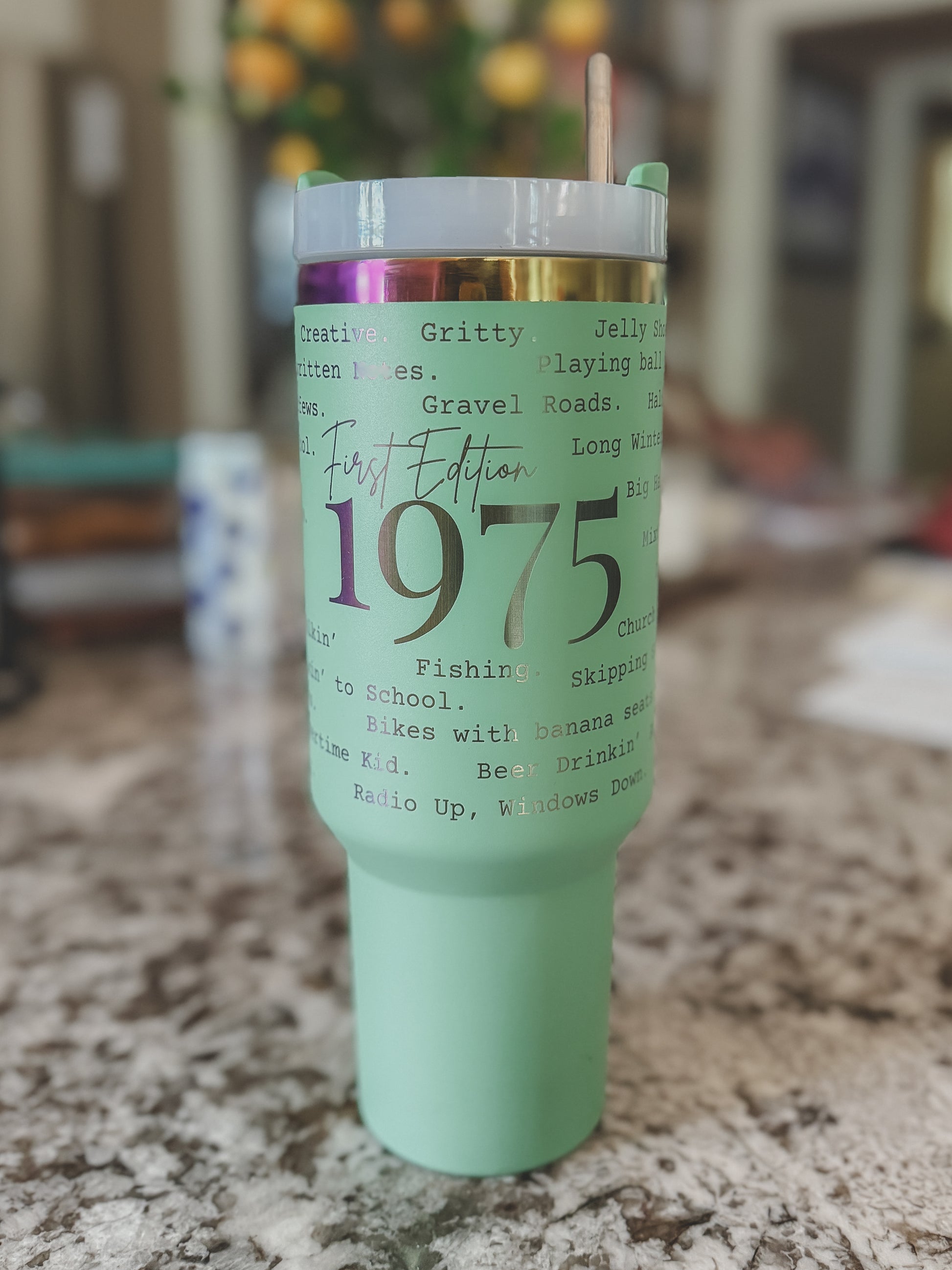 Mint green and iridescent 40oz tumbler with custom 1975 phrases, sitting on a marble countertop

