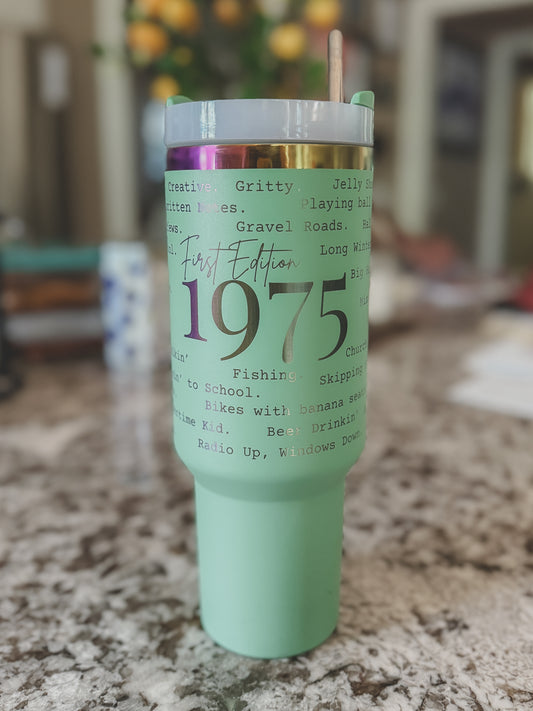 Mint green and iridescent 40oz tumbler with custom 1975 phrases, sitting on a marble countertop

