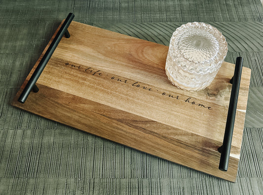 Acacia wood tray with black metal handles and engraved quote ‘our life · our love · our home’ styled with a clear candle jar
