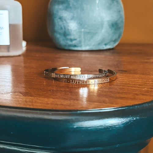 Custom engraved gold cuff bracelet with personalized name and quote, styled on wood surface