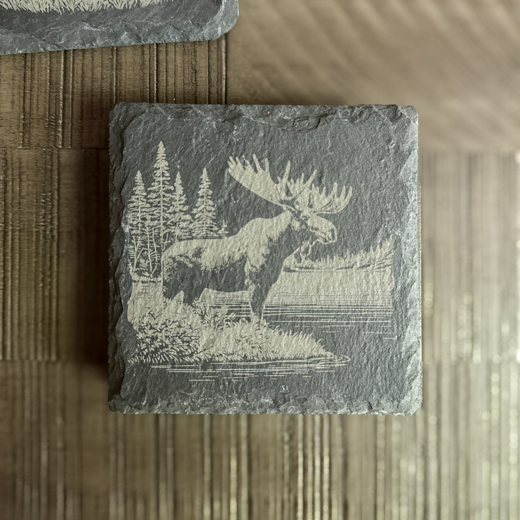 Engraved moose on slate coaster with pine trees – handcrafted cabin decor.