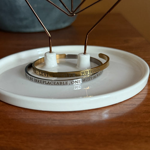 Two custom engraved cuff bracelets with names and quotes on a white dish and wood surface background