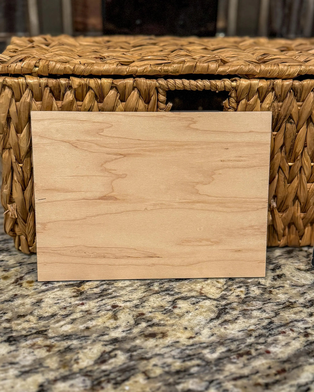 Back of the engraved wooden recipe card showing the natural woodgrain, placed on a granite surface in front of a wicker basket