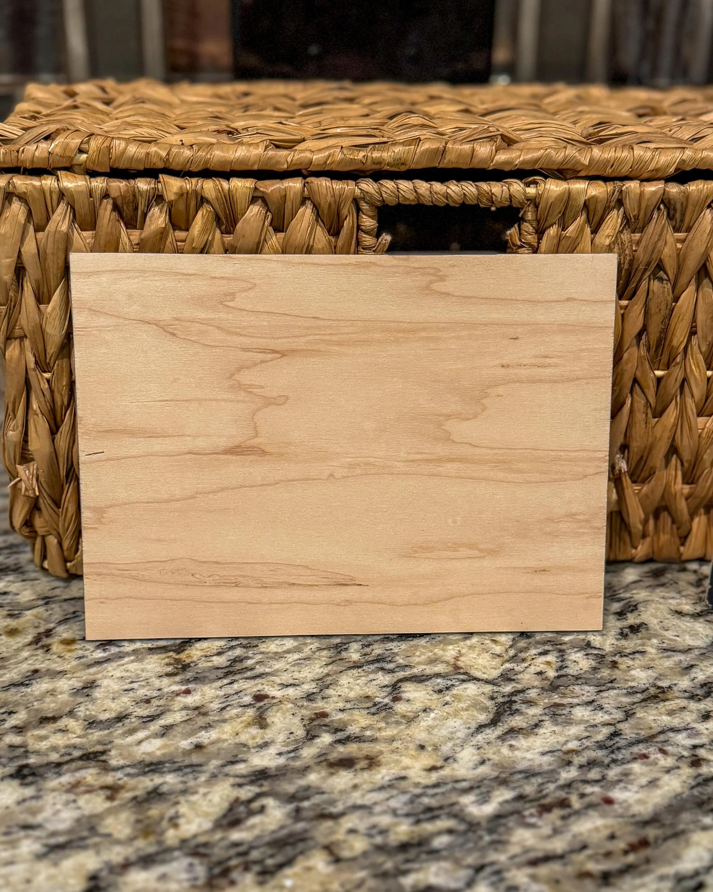 Back of the engraved wooden recipe card showing the natural woodgrain, placed on a granite surface in front of a wicker basket