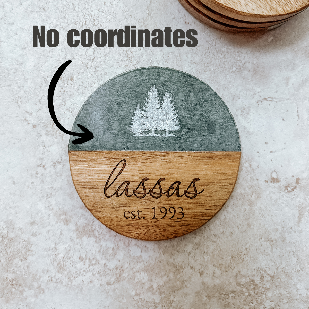 Personalized round wooden coaster with evergreen tree design and 'Lassas est. 1993' engraving on a two-tone surface.