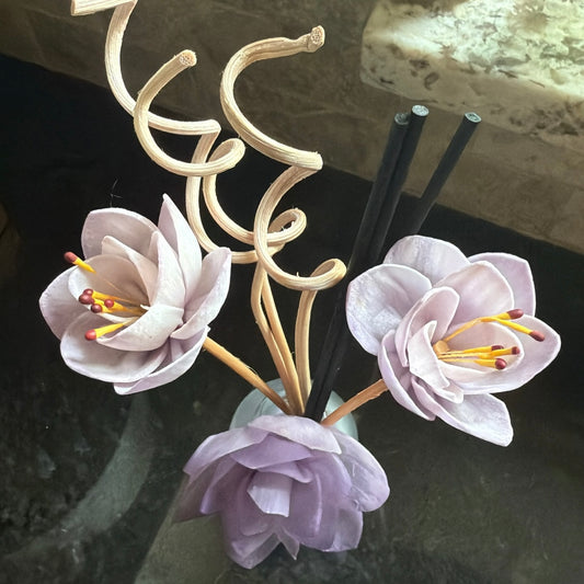 Lilac Bloom reed diffuser with floral decorative sticks and black reeds on a dark stone surface