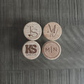 Top view of four engraved wooden wine corks with custom initials and monograms on a textured dark surface.